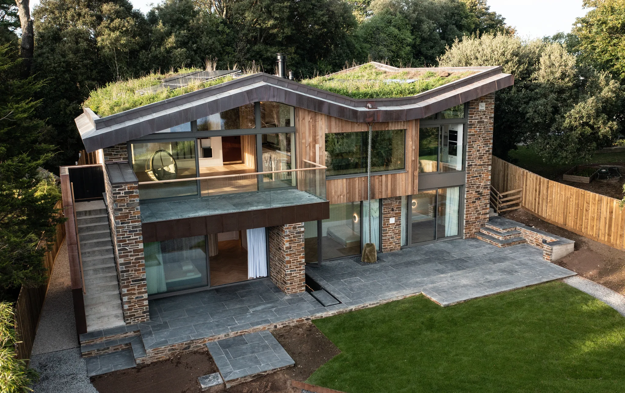 Aerial view of a modern house with a green roof and stone patio surrounded by trees