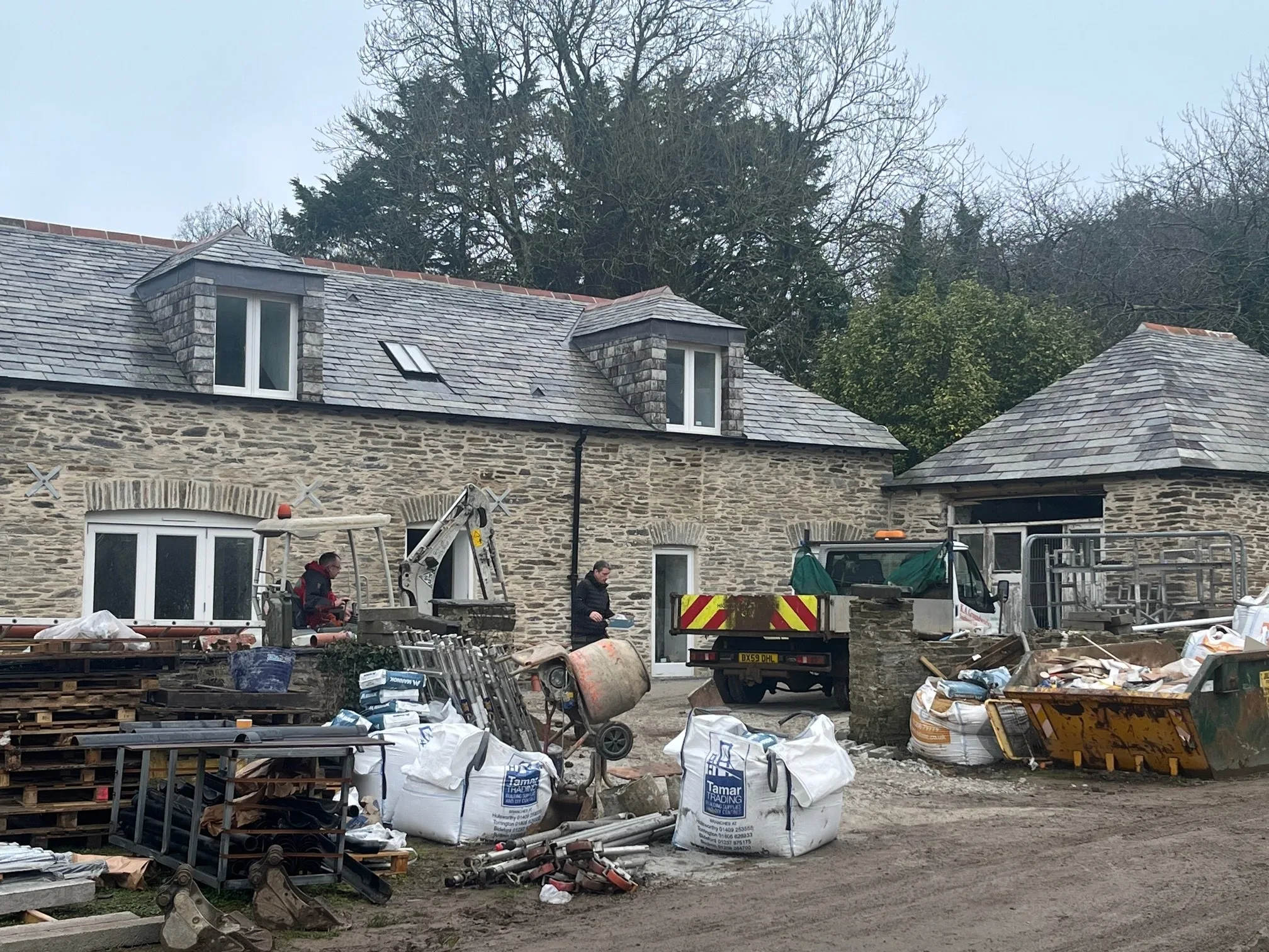 Stone cottage with slate roof under construction with building materials and equipment outside