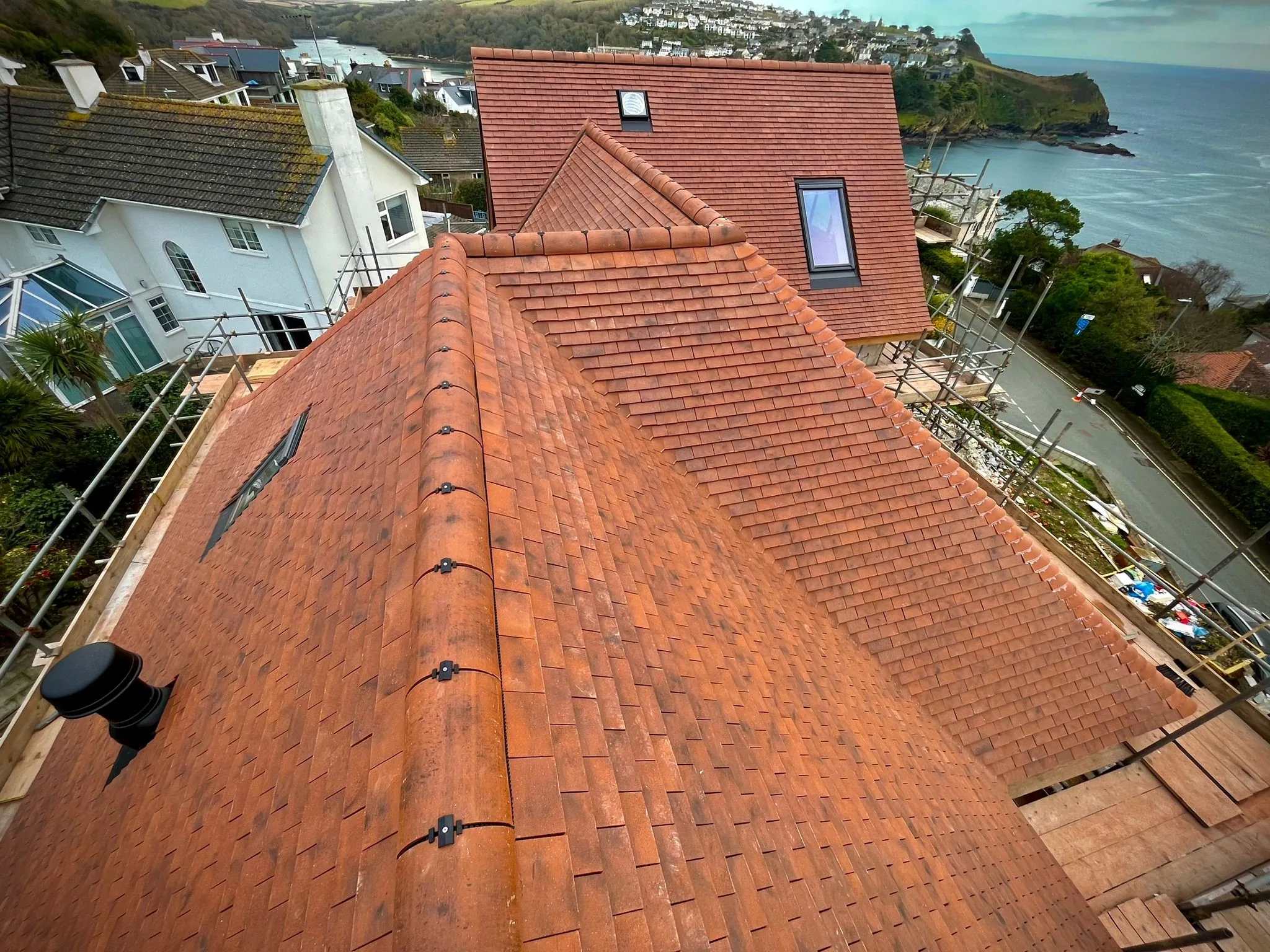 Freshly installed red clay tile roof with ridge tiles overlooking coastal houses and sea